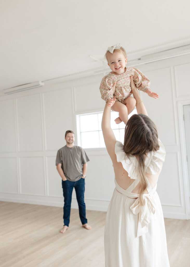oklahoma studio maternity photographer, mom in white dress throwing toddler while taking pregnancy photos