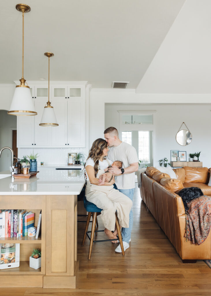 Wide photograph of the family's kitchen, lounging at the bar holding their newborn baby boy