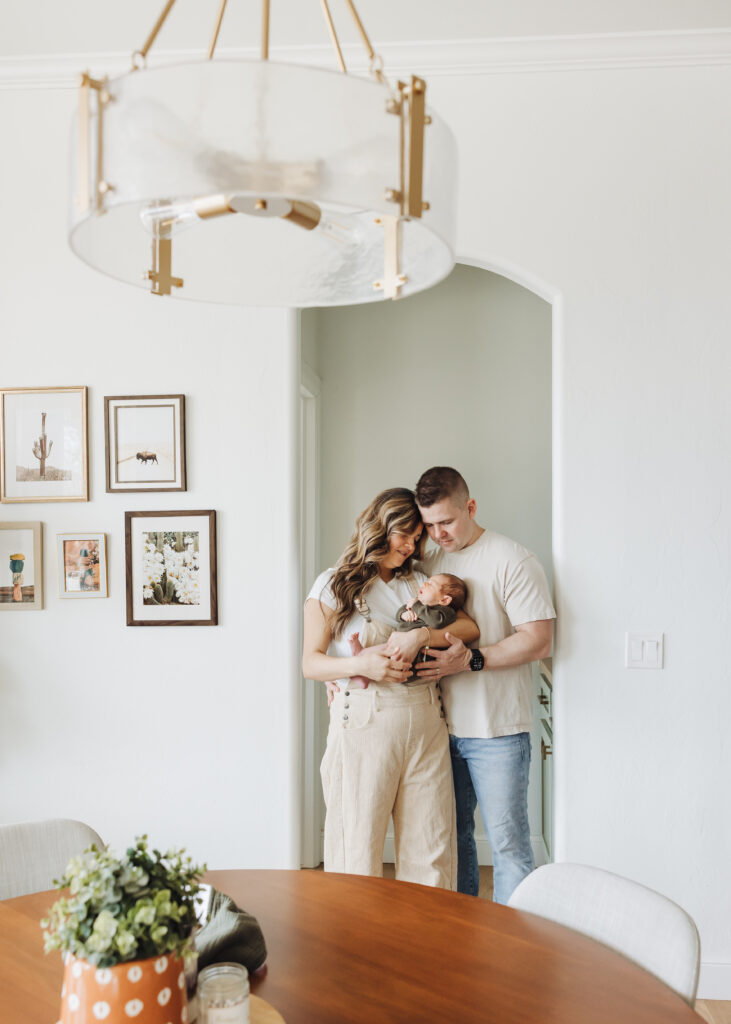 Photo of a family of 3 standing in their dining room with their new baby